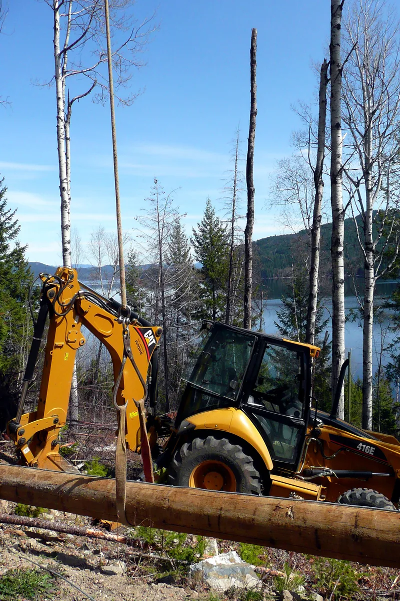 CAT backhoe excavator clearing trees on a lakefront lot in Muskoka cottage country with lake and forested hills in background